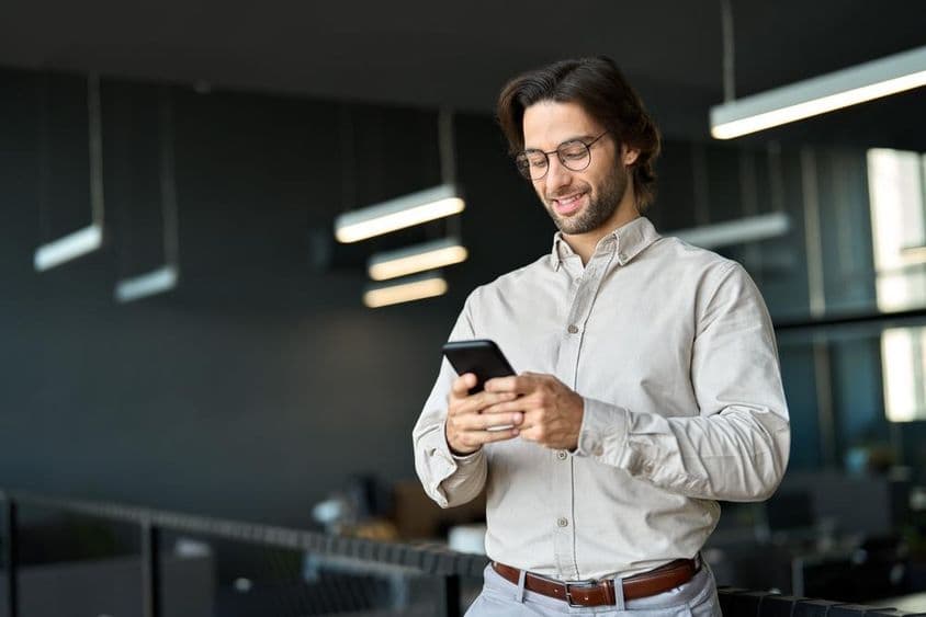 Young European business man using cellphone at work standing in office.