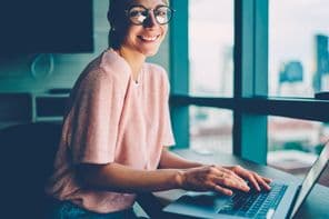 A happy young woman is programming on a computer.